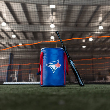 Blue Jays gear bag with black baseball bat on turf in indoor training facility
