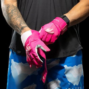 Bright pink baseball batting gloves with white accents, worn by a player with tattoos.