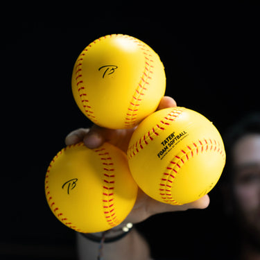 Hand holding three yellow Tater foam softballs, two showing the TB logo